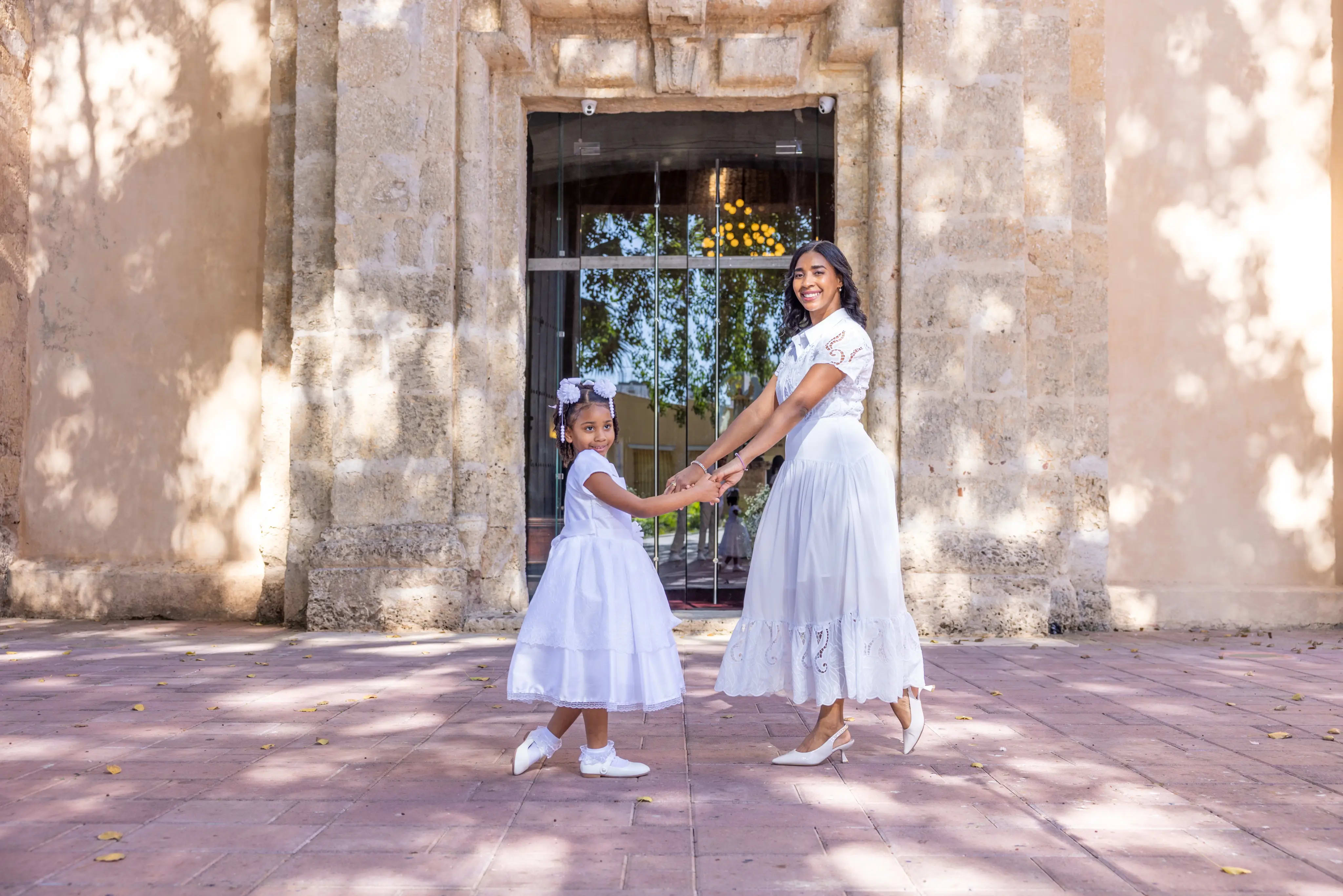 Madre e hija vestidas de blanco caminando tomadas de la mano en la entrada de la iglesia colonial, Santo Domingo — Babula Shots