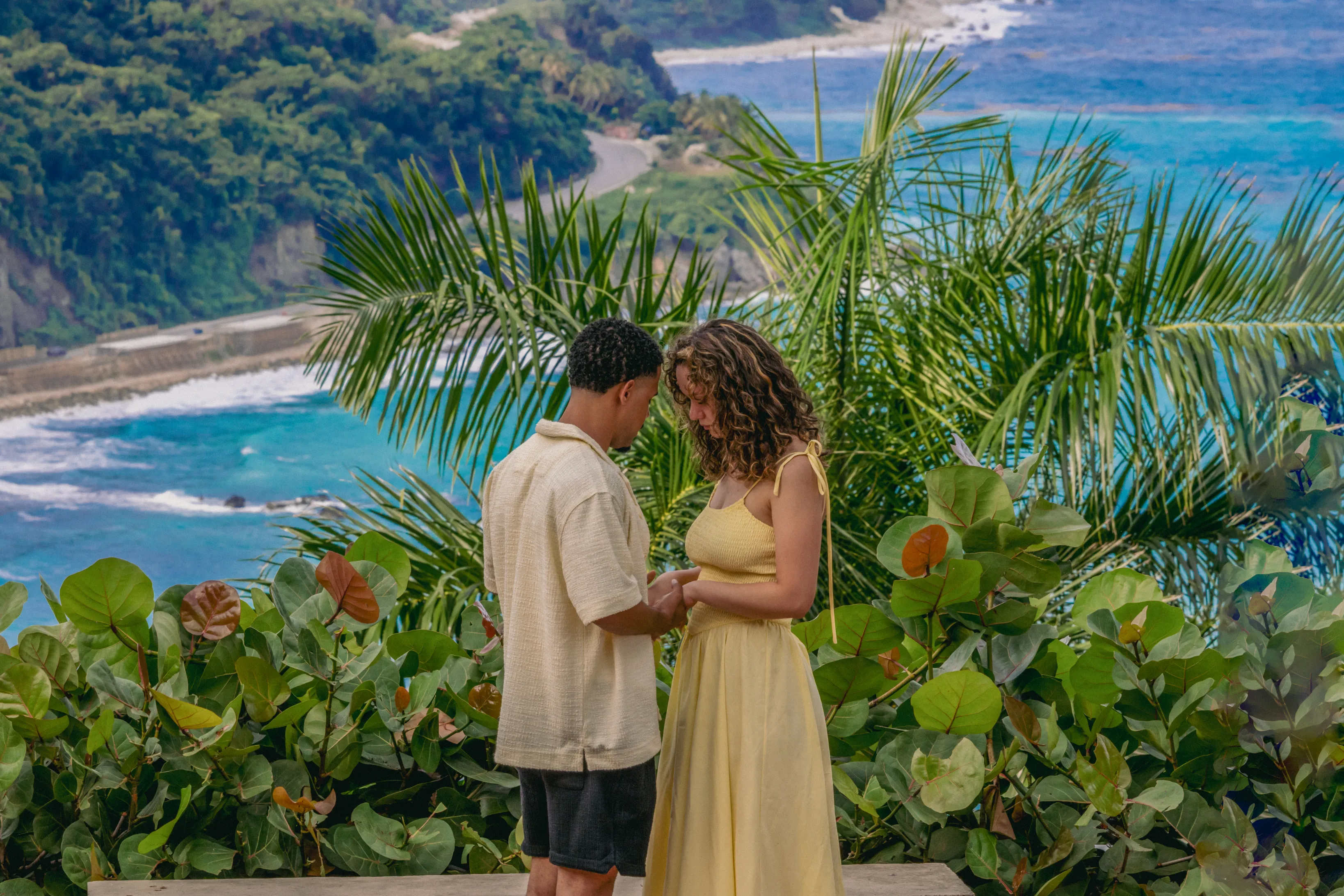 Pareja tomada de las manos con las frentes juntas, momentos antes de una propuesta sorpresa, con la costa turquesa cerca de Paraíso, Barahona de fondo