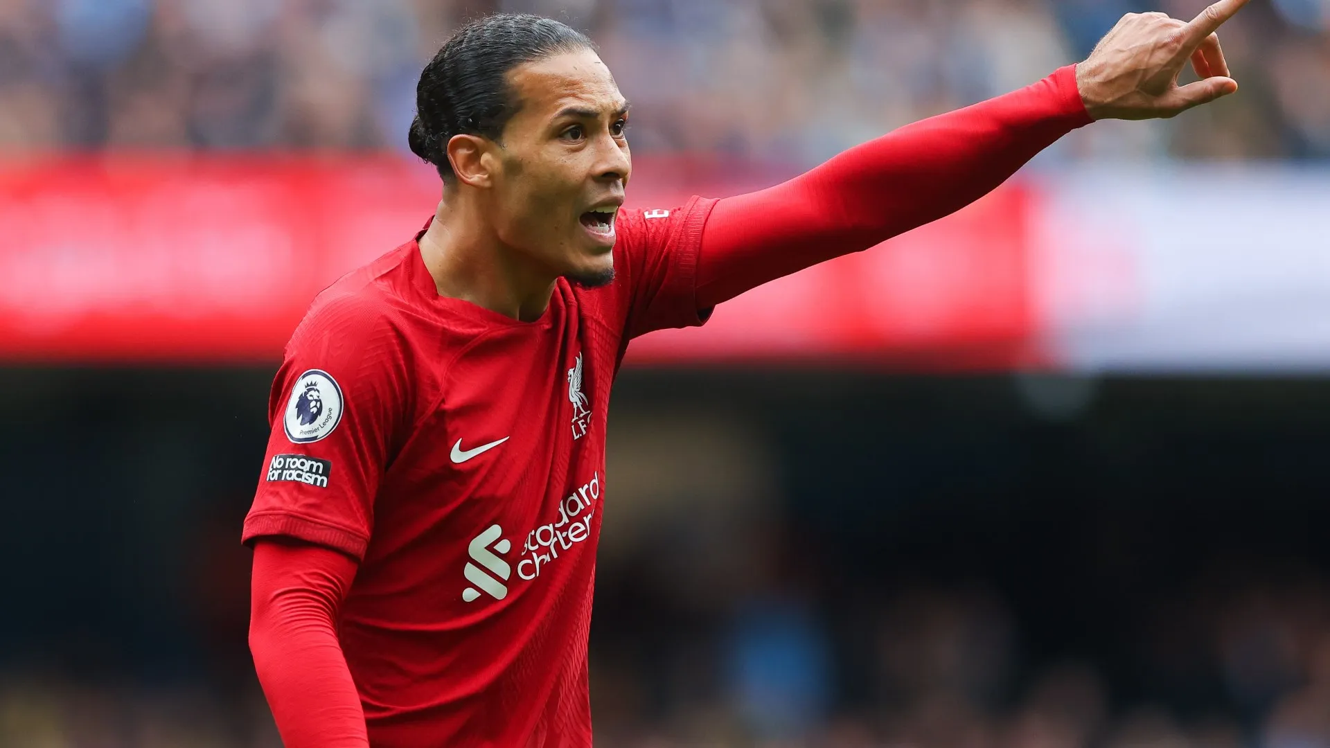 Virgil van Dijk mengangkat lengan memimpin rapat tim, latar belakang Anfield, tatapan tegas