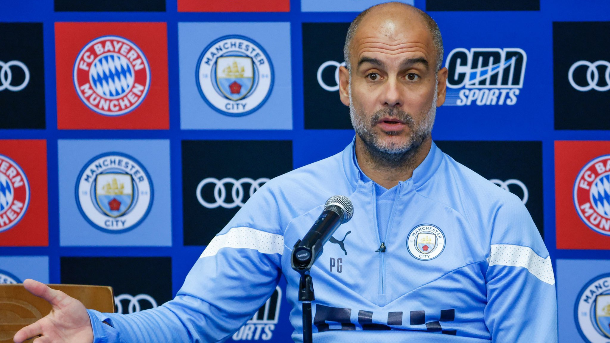 Pep Guardiola berbicara di konferensi pers, latar belakang layar dengan kutipan 'Play with belief, not fear'
