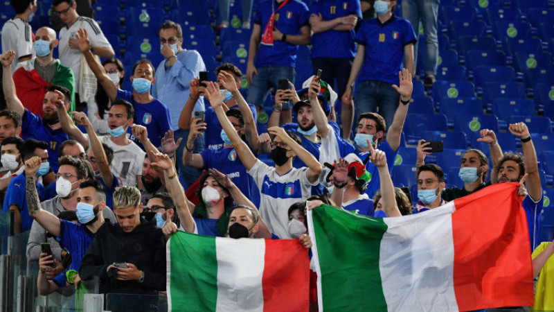 Suporter Italia memegang bendera Azzurri di stadion dengan ekspresi cemas
