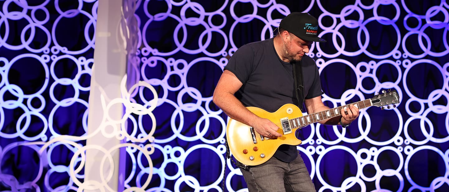 Tim Benniks playing a gold electric guitar on stage at ContentCon