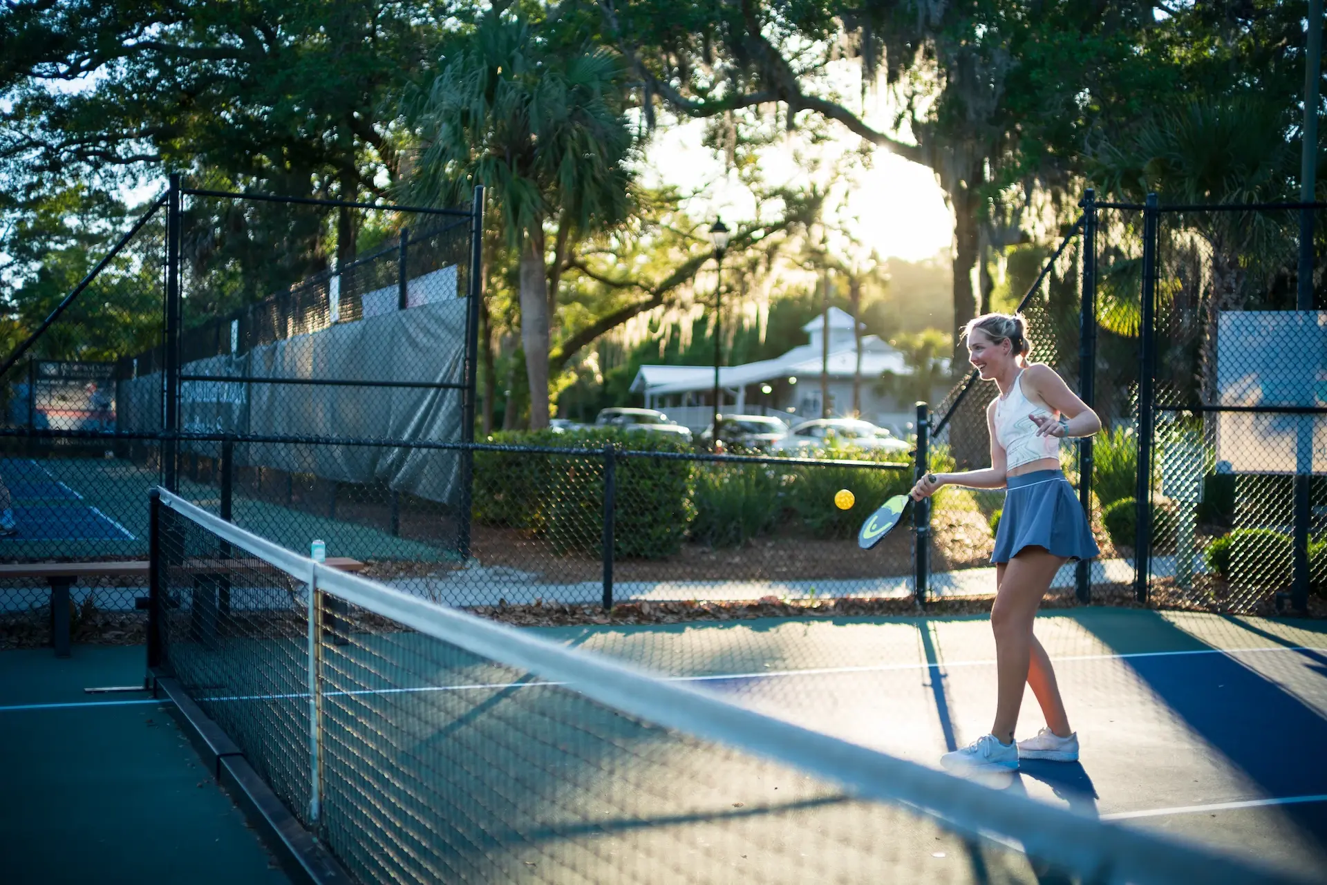 woman actively hitting the pickleball on the Palmetto Dunes pickleball course with the sun shining between the trees in the background