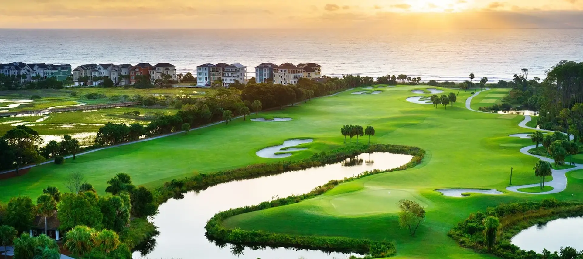 aerial view of the lagoon and golf course in front of the ocean with the sun rising over the water