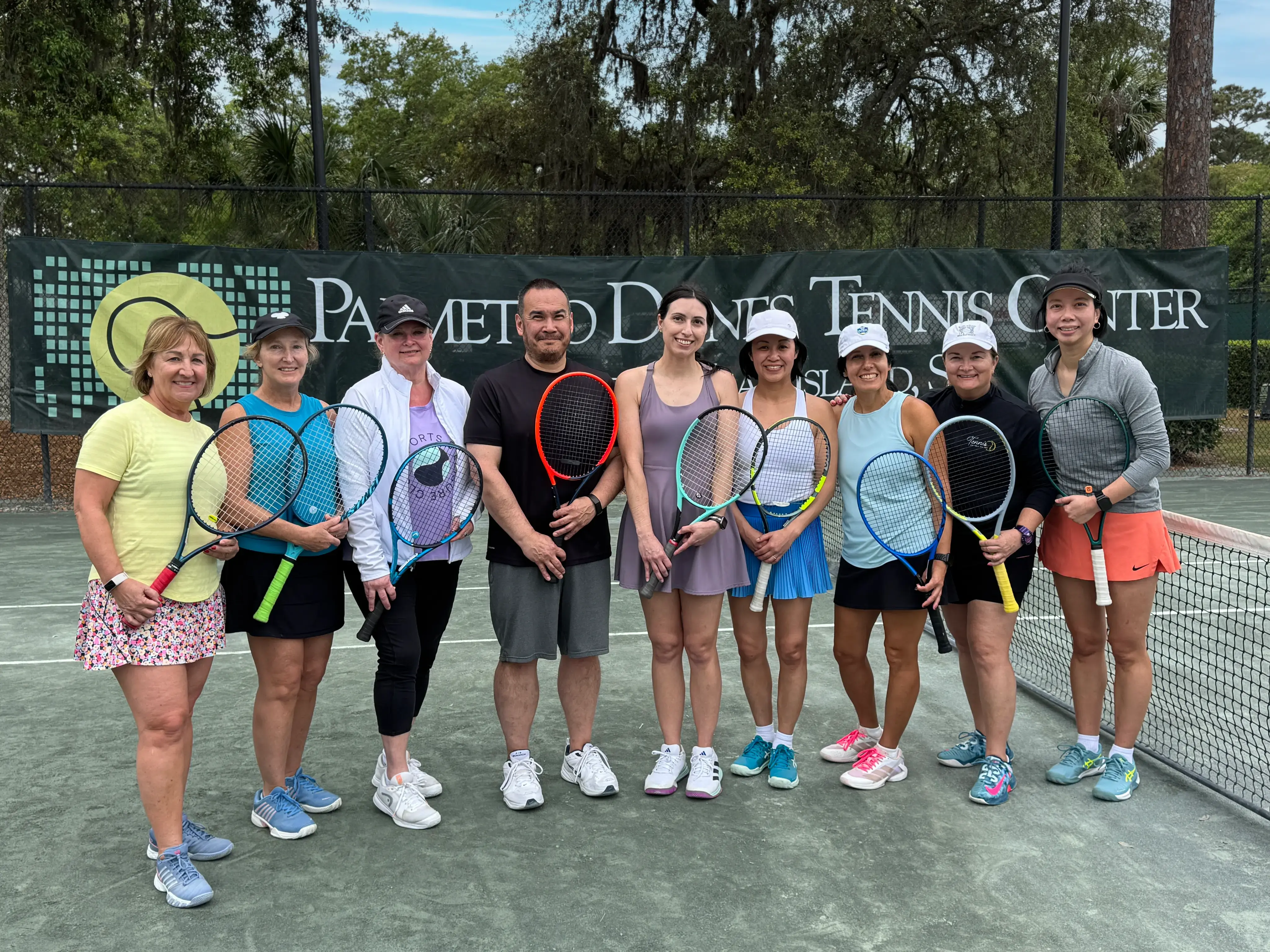 large group of tennis players pose with their rackets with the Palmetto Dunes Tennis center sign in the back