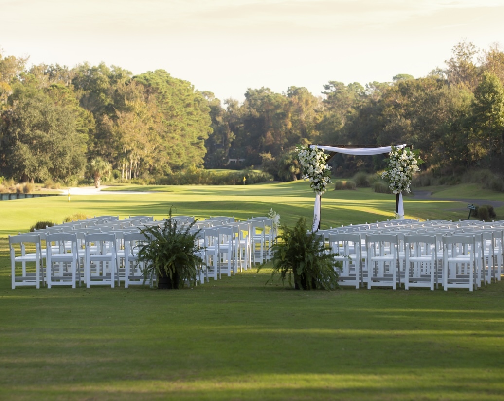 wedding ceremony setup on the greens of Arthur Hills golf course with a wooden arbor and green floral arrangements