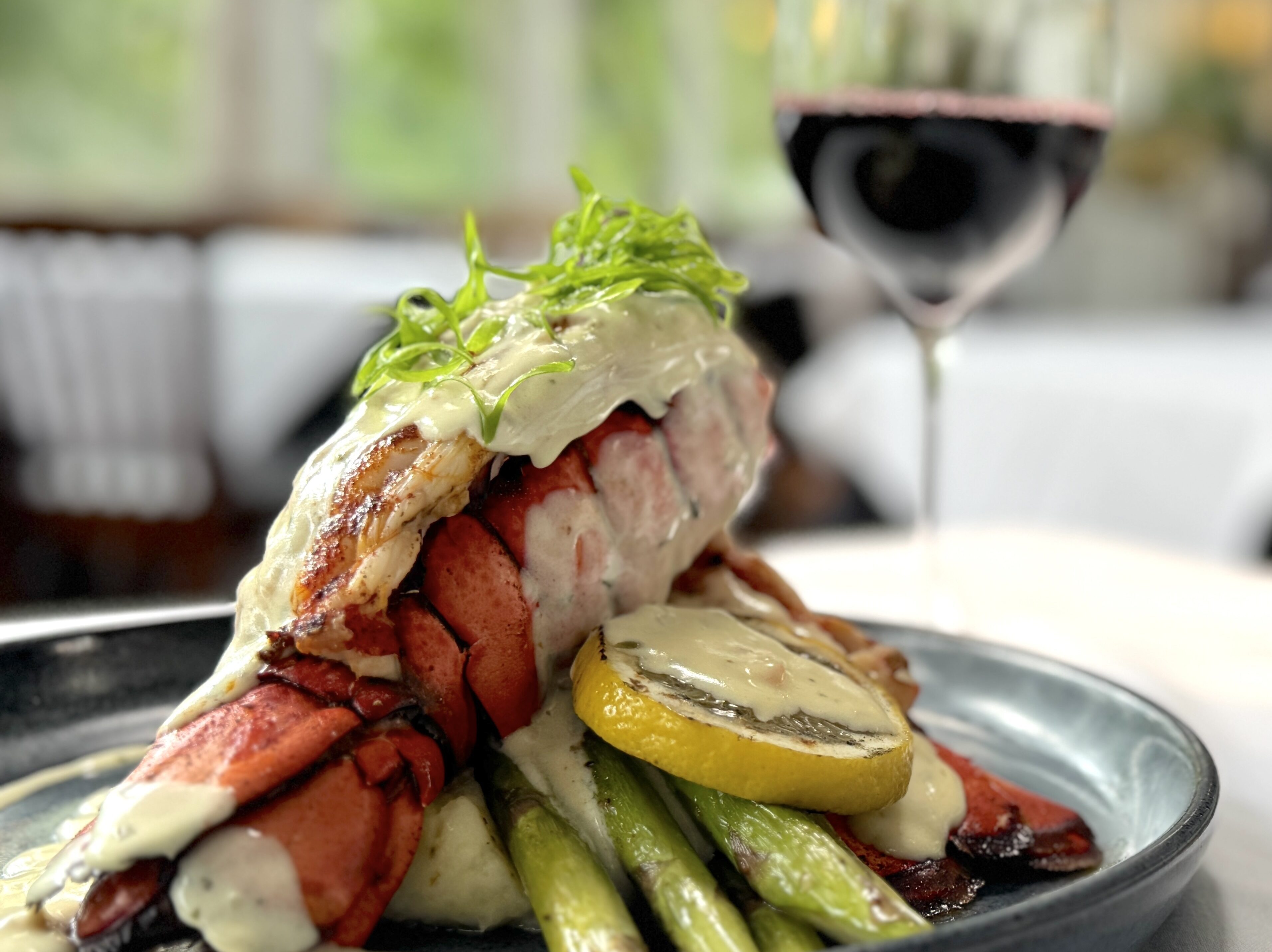 lobster tail over asparagus and lemon with a glass of red wine in the background