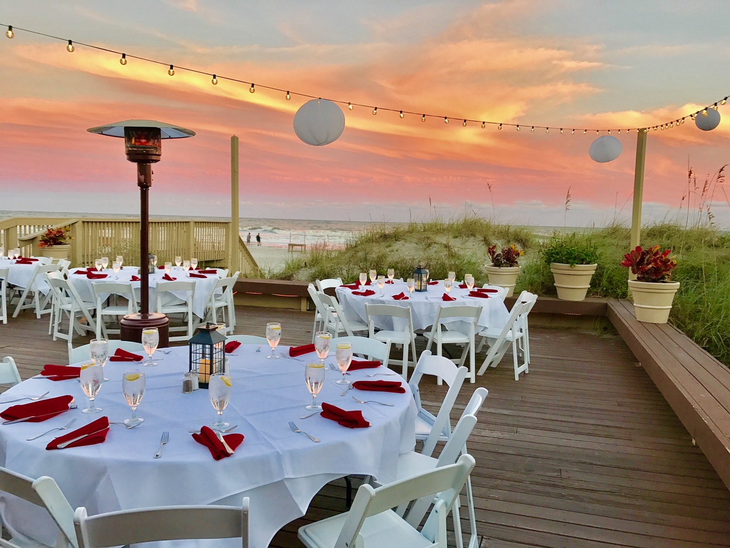 white round tables with red napkins set up on the deck of the Dunes House for a wedding with pastel skies during sunset