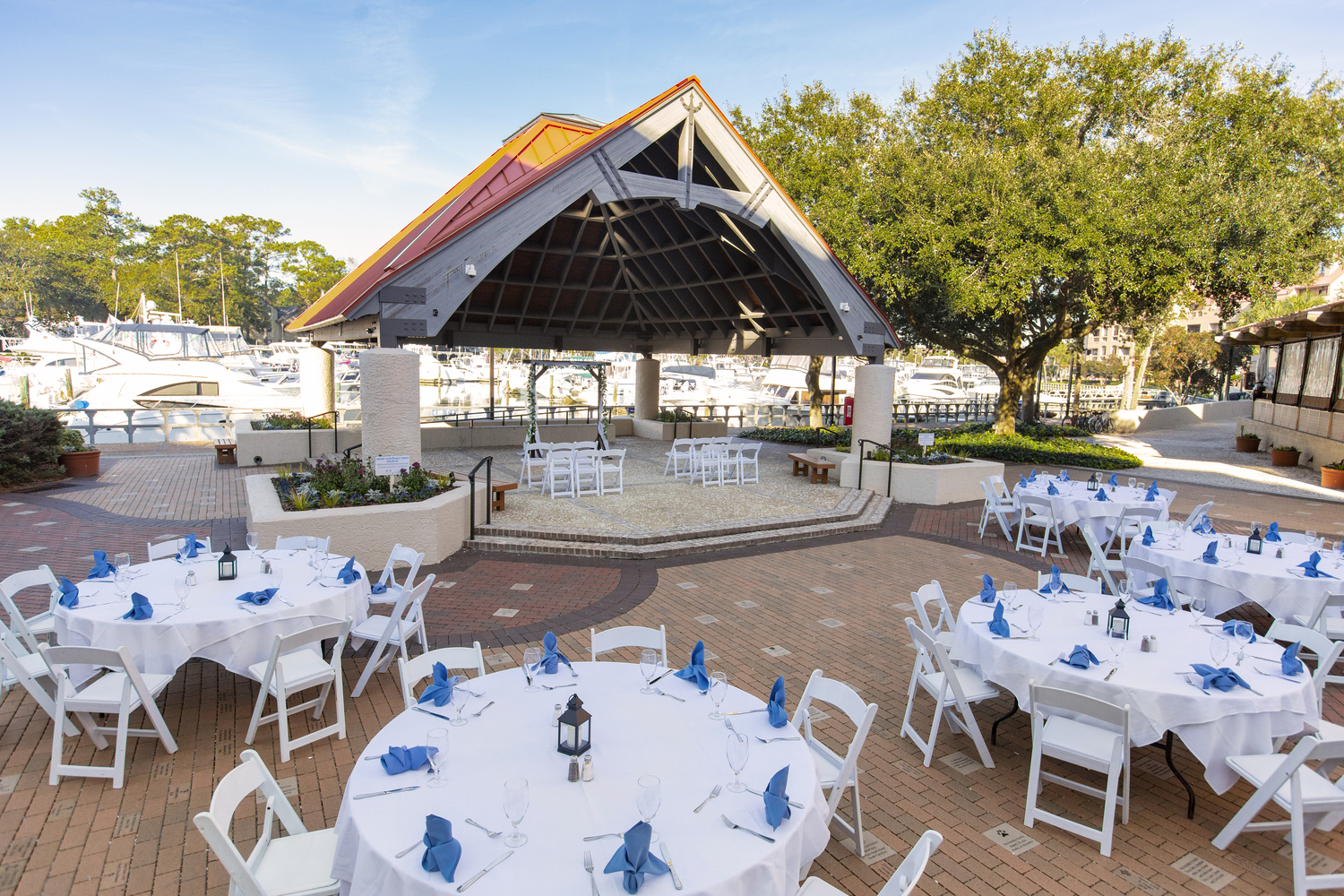 several round white tables set up with blue napkins next to the Shelter Cove Harbour & Marina pavillion