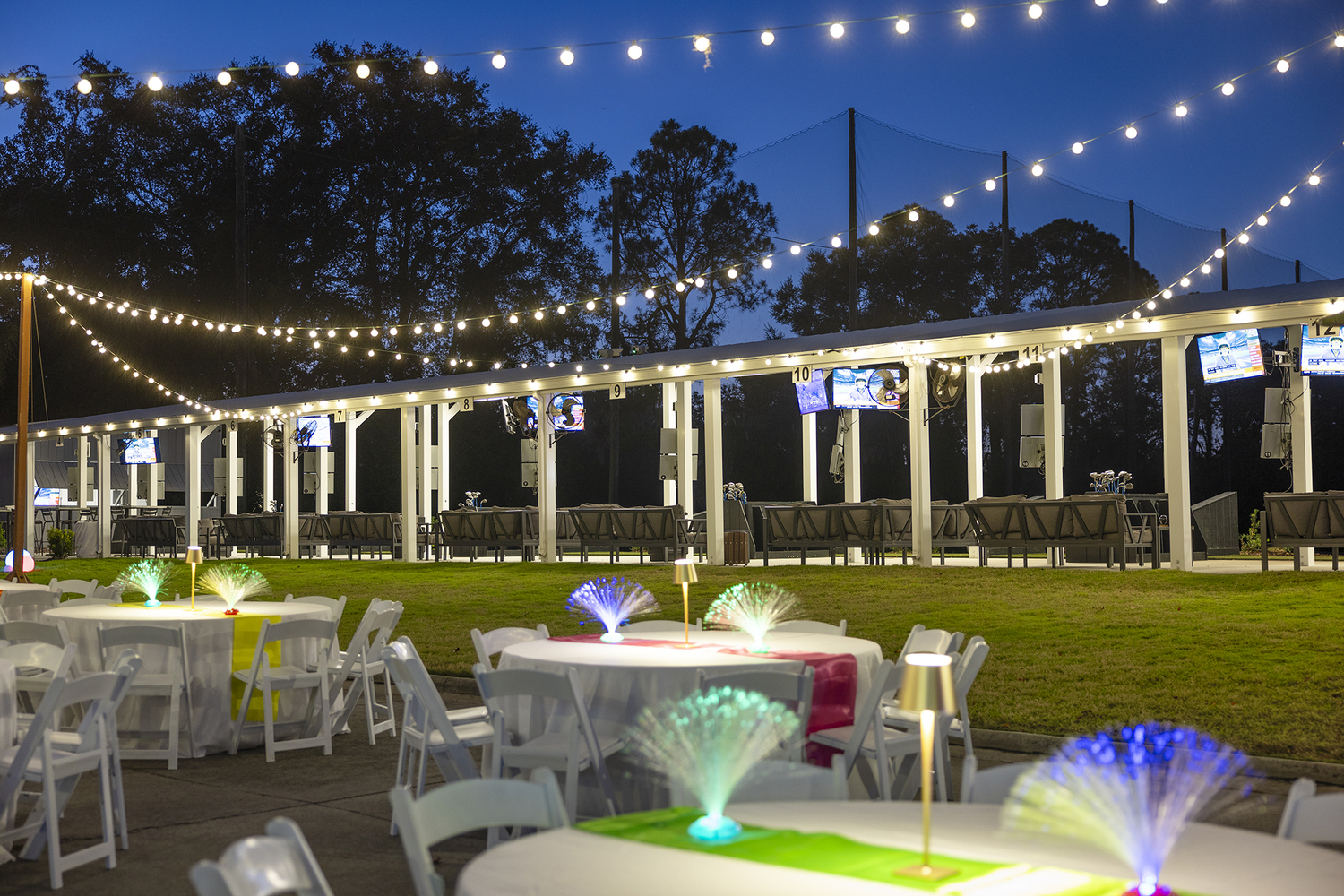 Toptracer driving range set up at night with string lights hanging above and fiberoptic lights set up on white round tables at night