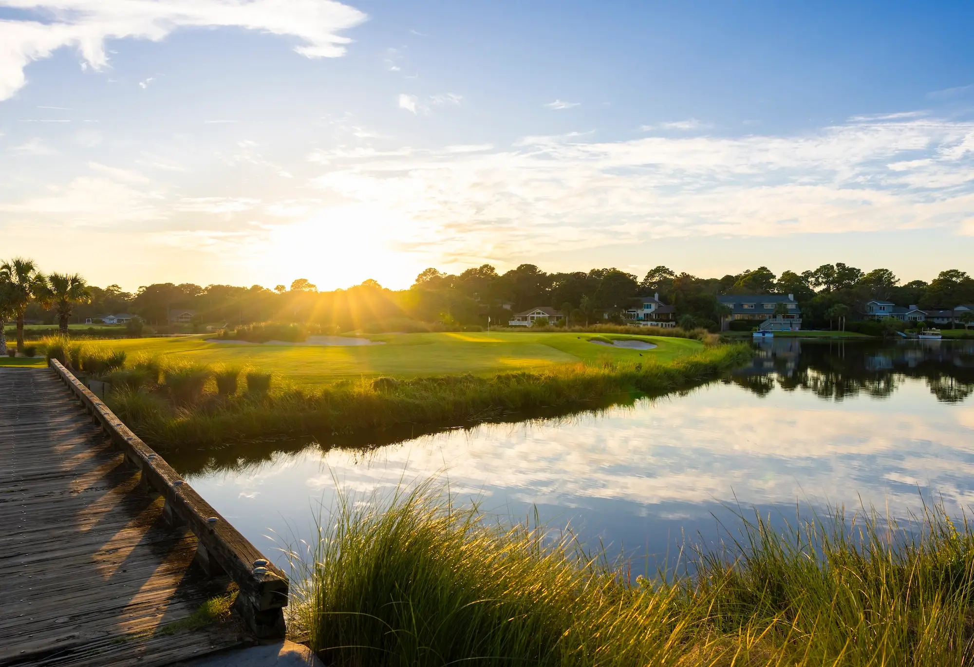 sun rising over the horizon over a bridge next to water and golf course