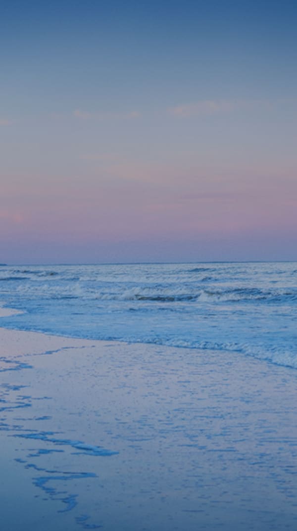 a couple embrace each other as they walk along the water of Palmetto Dunes beach with cotton candy skies at sunset
