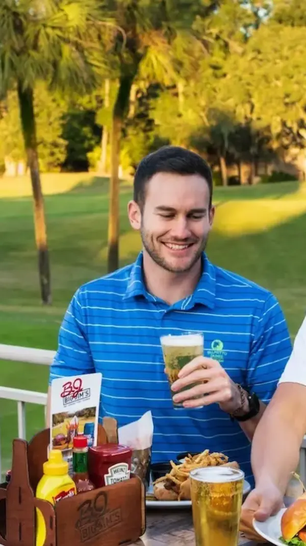 group of male golfers enjoy food and drinks on the Big Jim's deck overlooking the golf course while a Big Jim's server puts a plate of food down