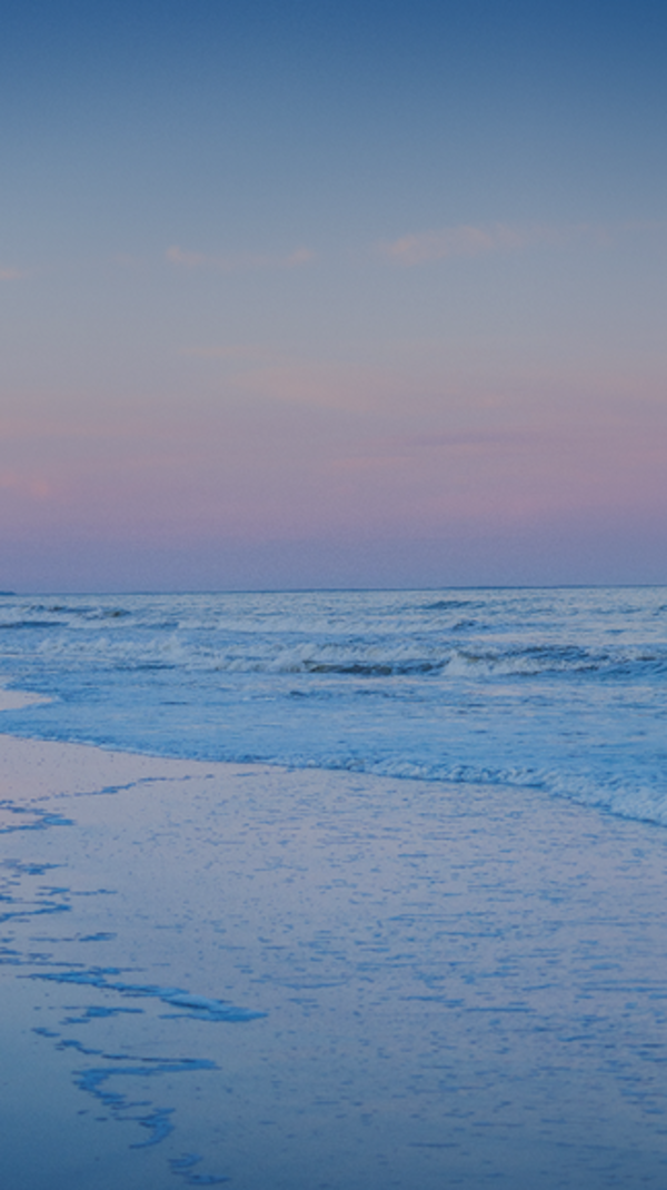 a couple embrace each other as they walk along the water of Palmetto Dunes beach with cotton candy skies at sunset