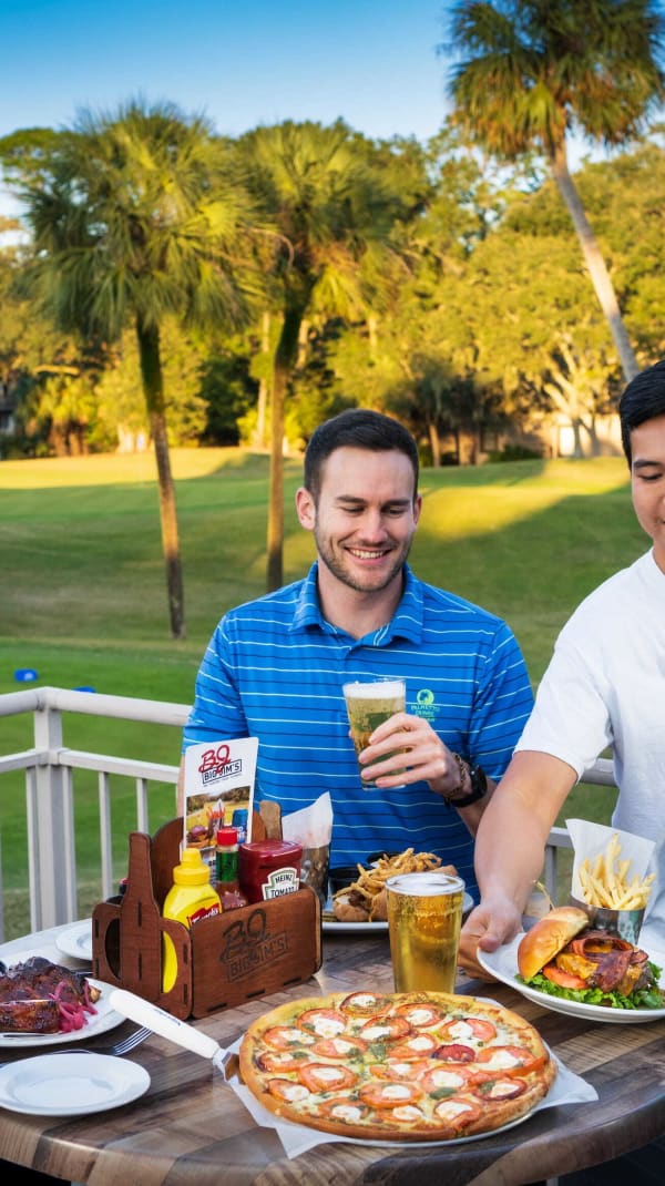 group of male golfers enjoy food and drinks on the Big Jim's deck overlooking the golf course while a Big Jim's server puts a plate of food down