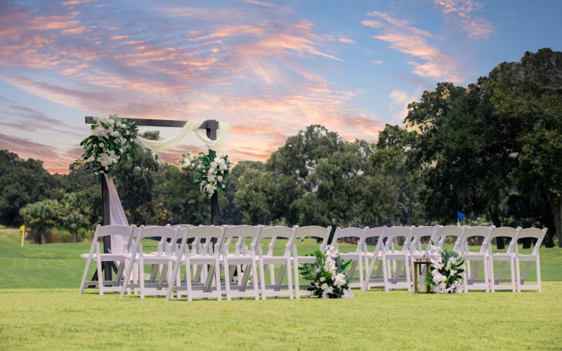 wedding ceremony setup with white chairs and a wooden arbor with flowers under a pastel sky