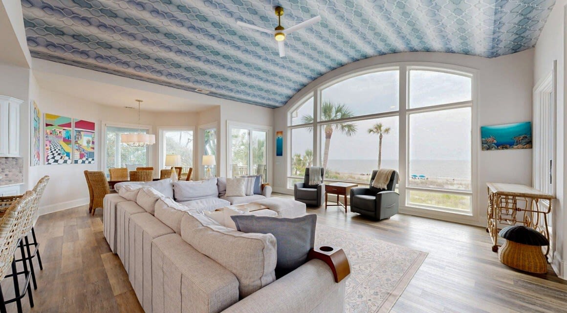 coastal living room with large windows overlooking the ocean and a blue wallpaper ceiling
