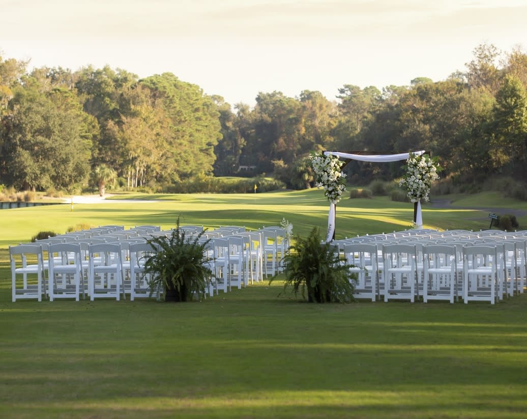 wedding ceremony setup on the greens of Arthur Hills golf course with a wooden arbor and green floral arrangements