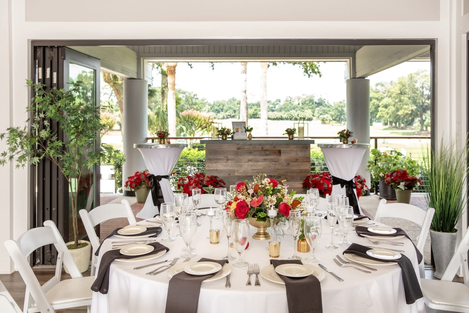 white round table with red and gold decor setup with two cocktail tables and a bar in the background of the open air porch