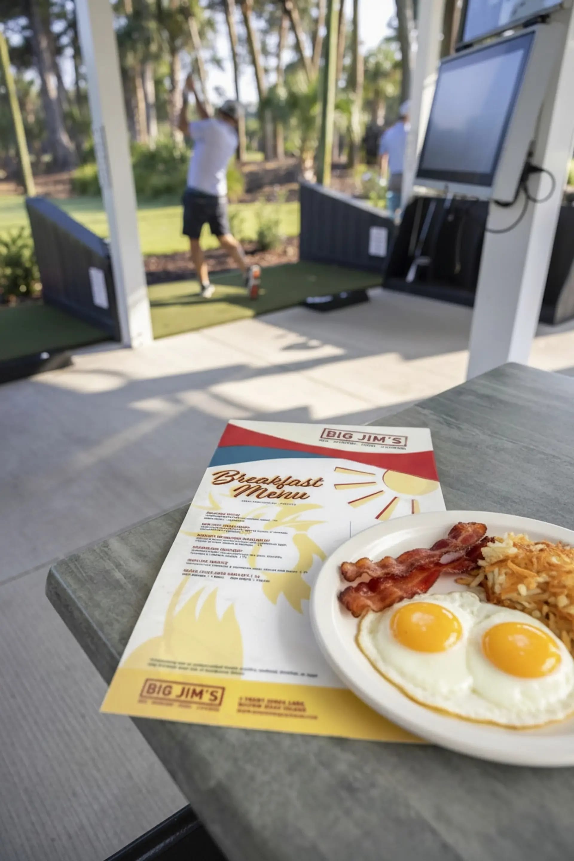 Eggs, bacon, and hashbrown on a table with a golfer swinging in the bay at Toptracer