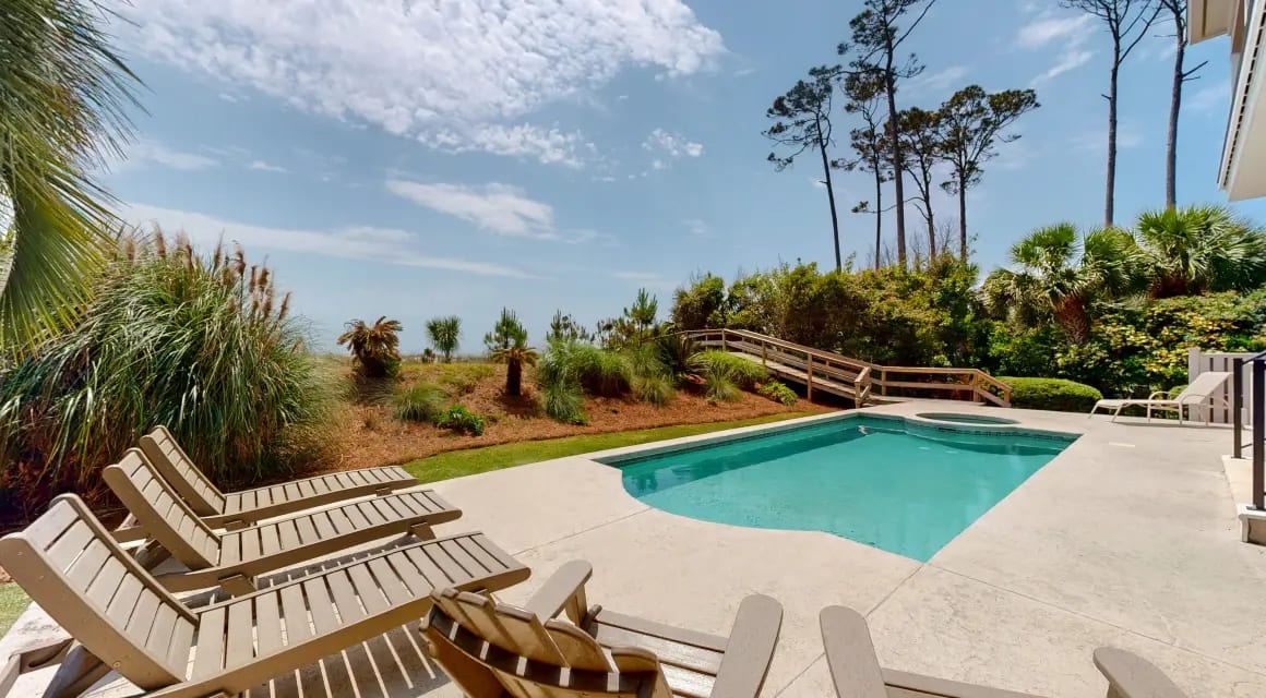 private pool and spa of a vacation rental home with lounge chairs next to the ocean dunes under a sunny sky