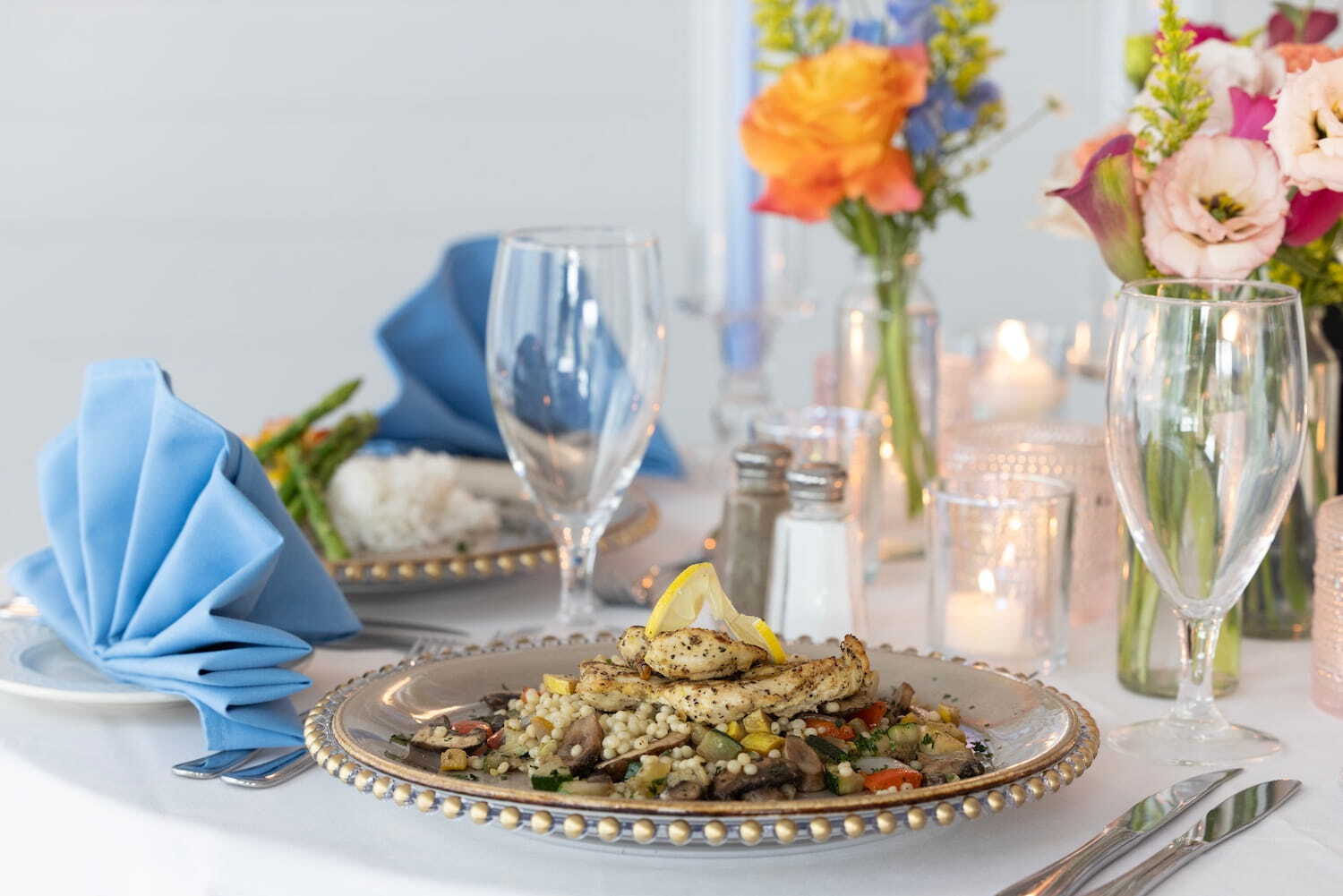 chicken dinner plate set on a tablescape with blue napkins and vibrant flowers