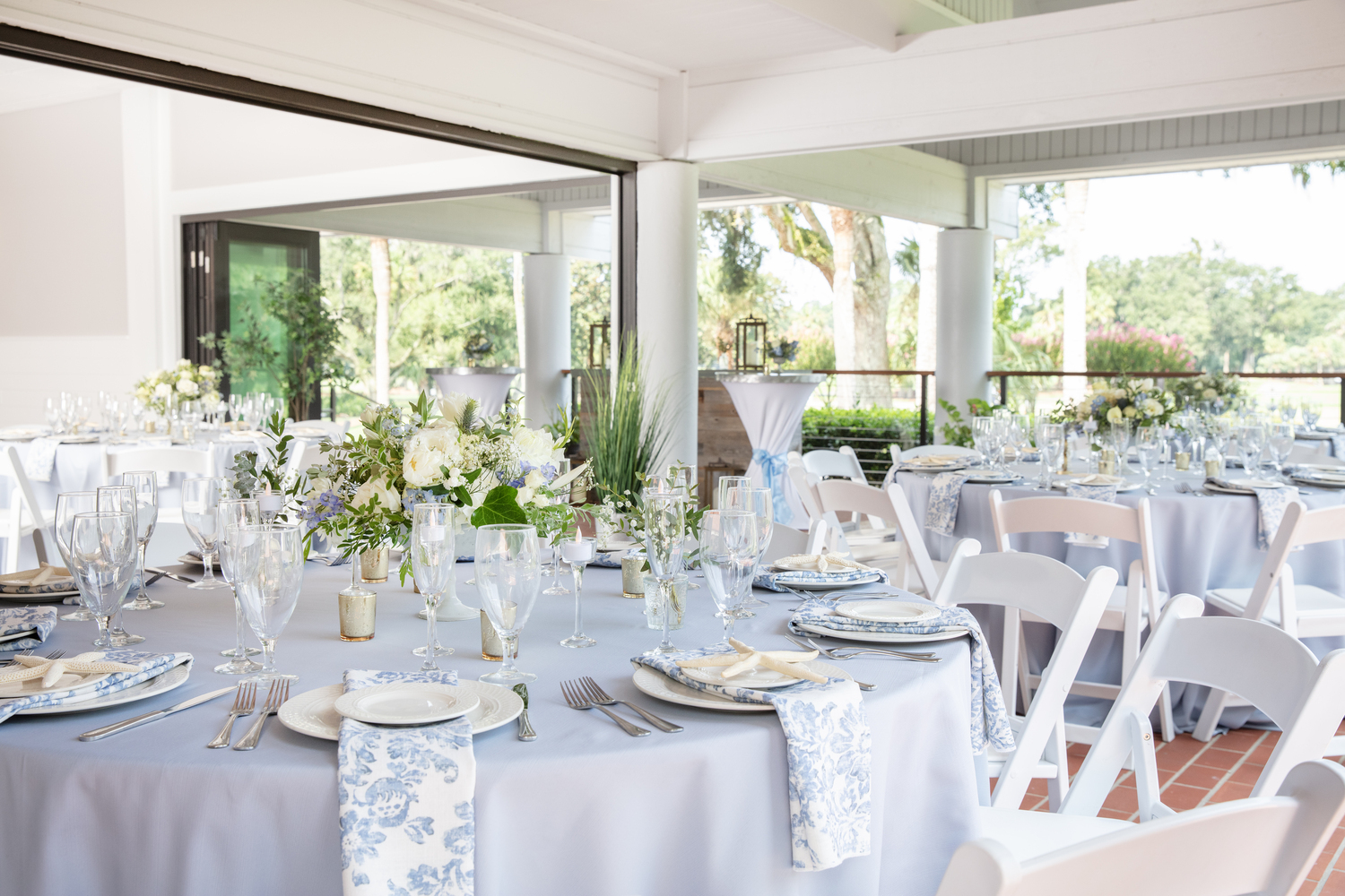 blue round tables with light blue tablecloths and coastal napkins set up for an event in the open air deck