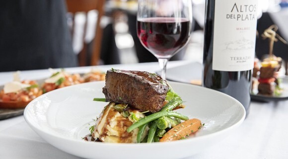 close up of steak overtop mashed potatoes and vegetables with a glass of wine