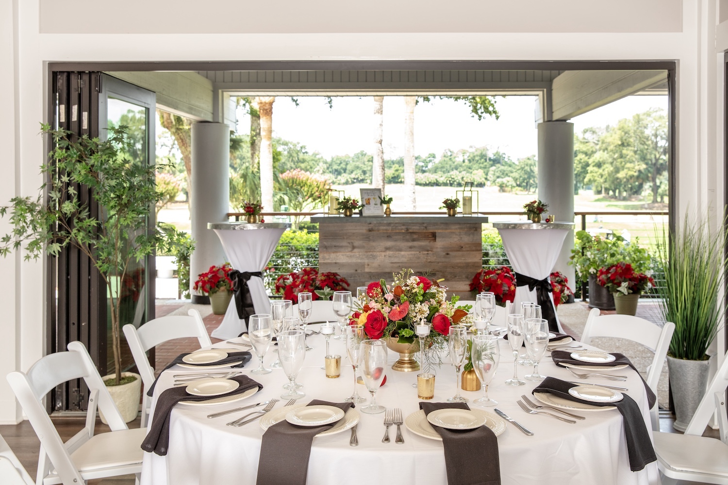 white round table with red and gold decor setup with two cocktail tables and a bar in the background of the open air porch