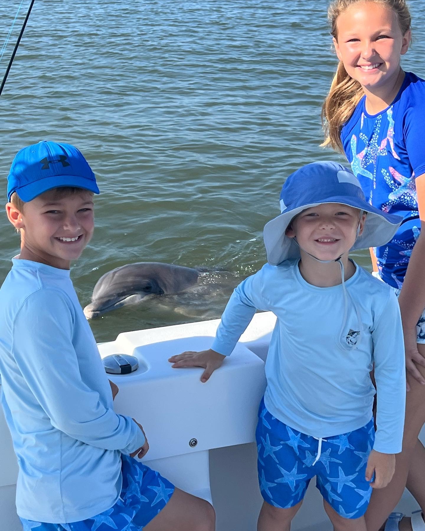 three young children pose next to a dolphin on the side of a boat