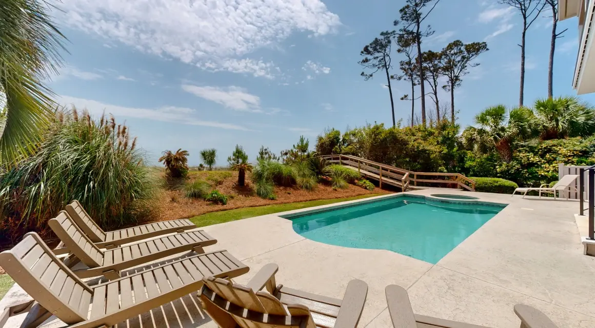 private pool and spa of a vacation rental home with lounge chairs next to the ocean dunes under a sunny sky