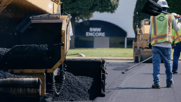 Fresh asphalt being laid and raked to grade by a paving crew.