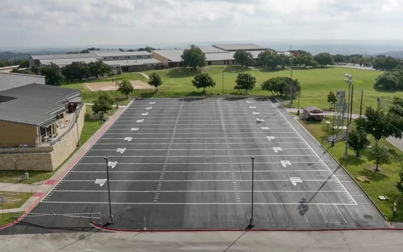 Sealcoat being spread in an even coat across an asphalt surface.