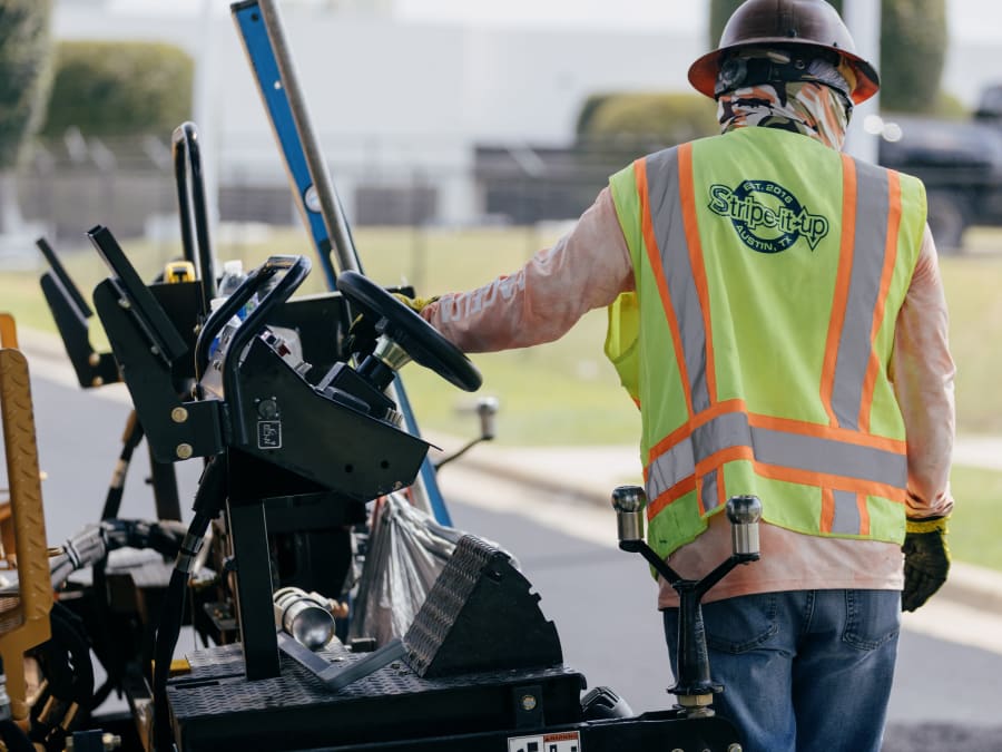 A crew member walking a line striping machine, laying fresh markings on pavement.