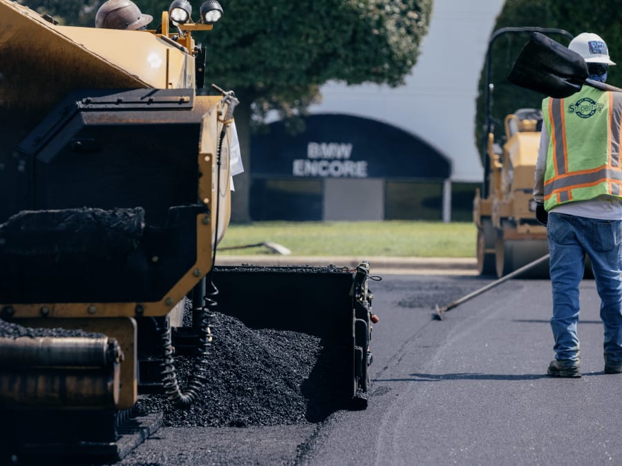 A paving crew raking and working hot asphalt behind the paver.