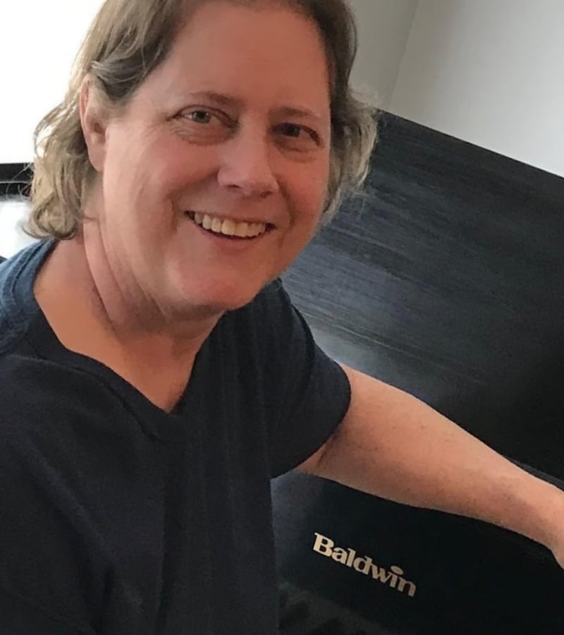 Victoria, music teacher at Piano with Victoria, smiling at the camera wearing a black Baldwin branded shirt.