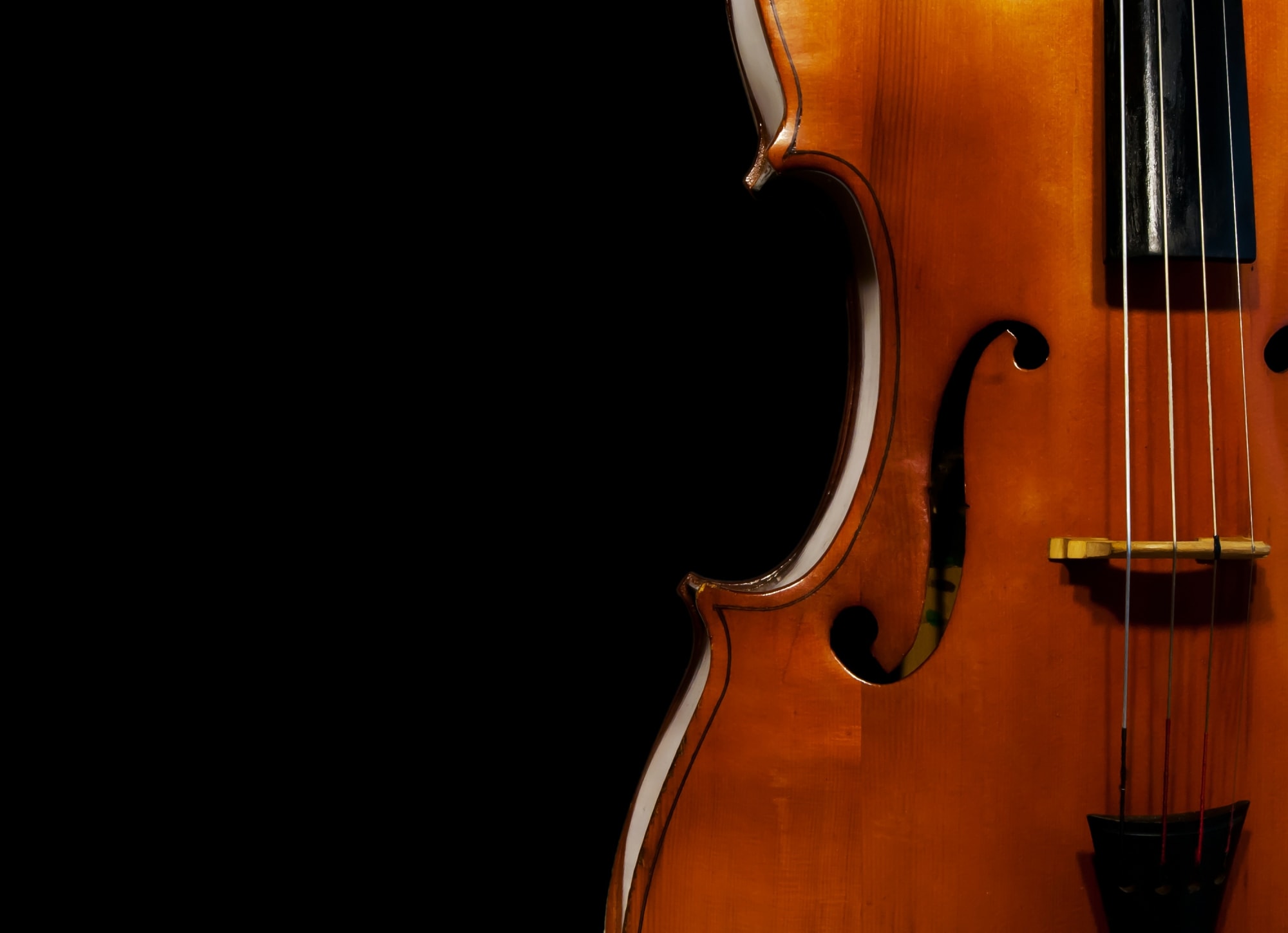Close-up of a wooden cello with four strings against a black background, showing the instrument's curved body and f-holes.