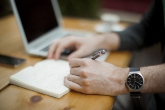 Person framför dator och anteckningsblock