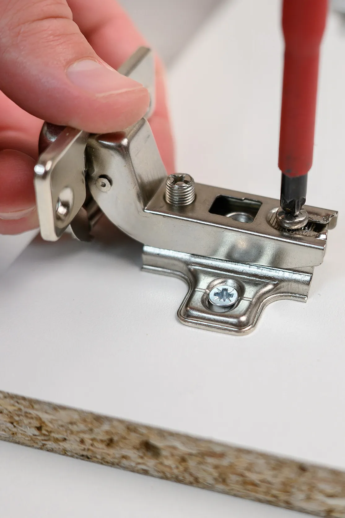 A worker is screwing a hinge into a wooden cabinet door with a screwdriver