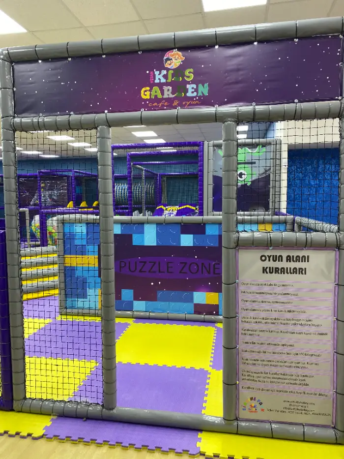 Aire de jeux douce avec panneau « Kids Garden Cafe & Game » et entrée « Puzzle Zone », où les règles de l'aire de jeux sont accrochées.