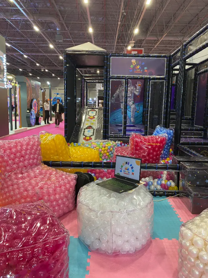 Fuar standımızdaki iç mekan oyun parkı, rengarenk top dolu puf koltuklar, laptoplu bir masa ve genel soft play kurulumunun geniş açılı görünümü.