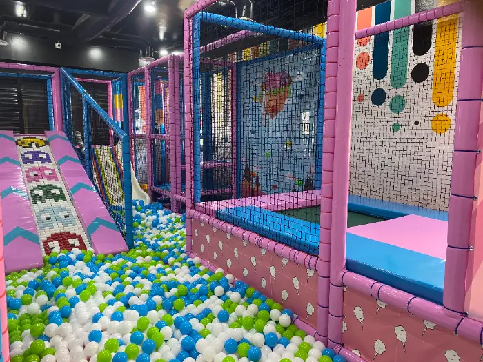 Pembe ve mavi temalı, rengarenk top havuzu ve kaydırak içeren geniş açılı soft play alanı görüntüsü.