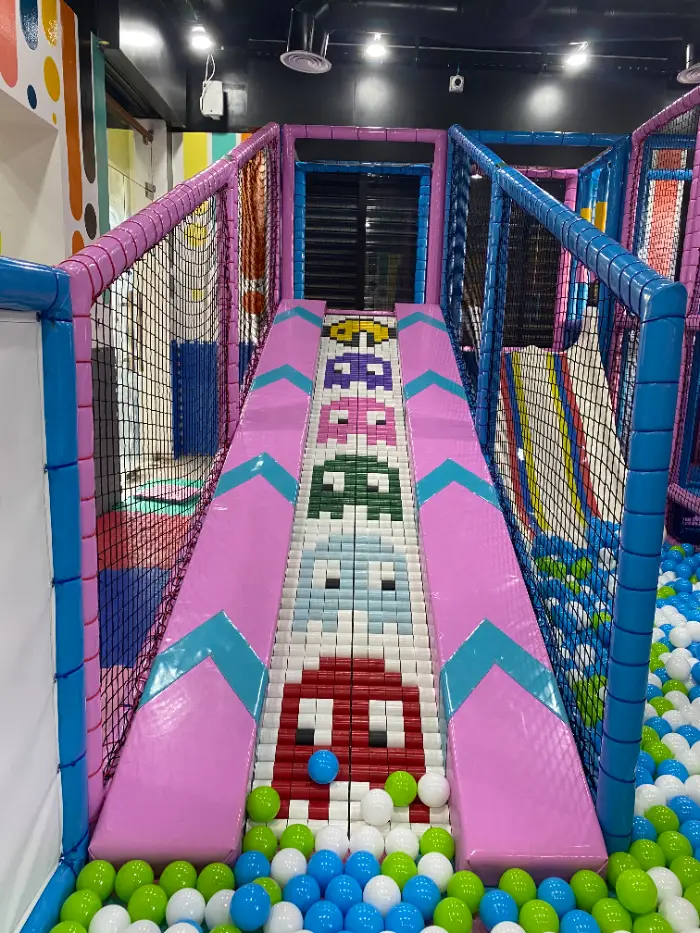 Yeşil, beyaz ve mavi toplarla dolu top havuzuna inen, Pac-Man temalı özel tasarımlı kaydırağın yakın çekimi.