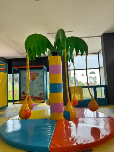 Çocukların etrafında dönebileceği, renkli minderli zemine sahip, tropik temalı soft play oyun alanı elemanı: palmiye ağacı.