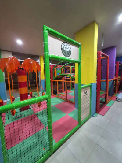Canlı renklerde tasarlanmış soft play alanının girişi, yeşil çerçeveli bilgilendirme panosu ve turuncu palmiye figürlü dekorasyonlarla birlikte.