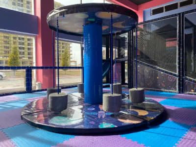 It is a spinning children's toy with a space-themed circular platform positioned in front of the outward-facing windows, surrounded by swing-like seats.