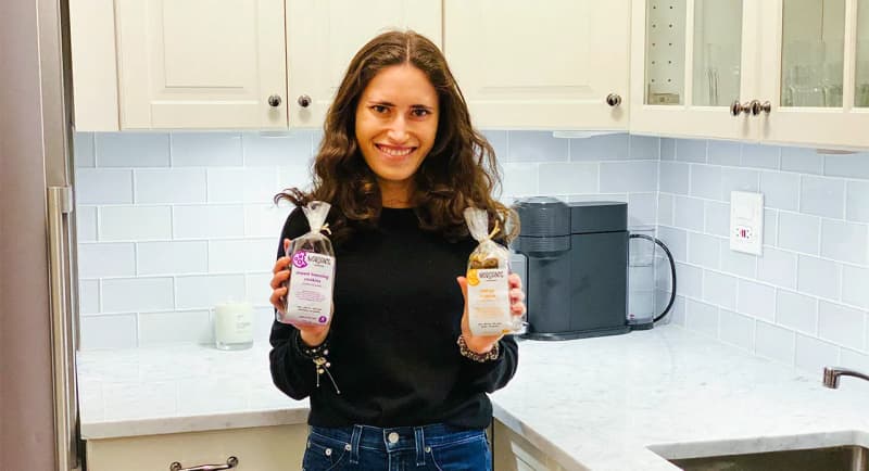 2015 Birthright Israel alumna Morgan Spindler in her kitchen holding up two packages of cookies from Morganic Bakeshop