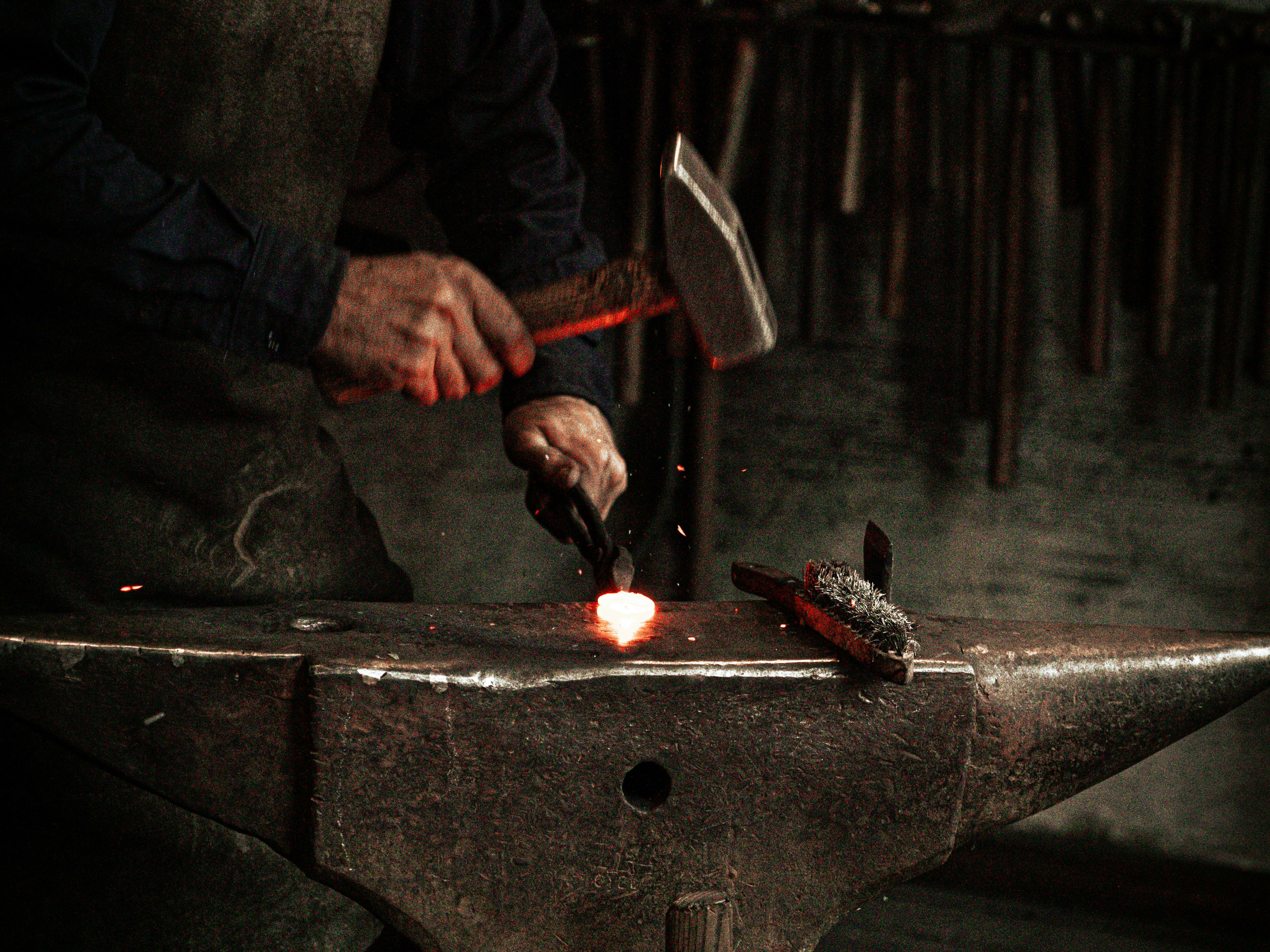 Blacksmith hammering hot tool on anvil.