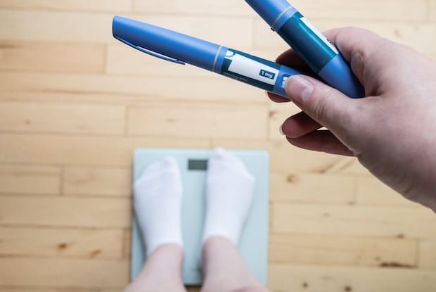 a person standing on a scale while holding several weight loss injection pens