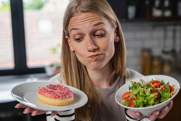 a woman deciding between a donut and a salad